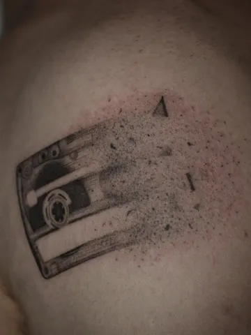 Kaseta magnetofonowa rozsypująca się w kropki, dotwork na ramieniu.