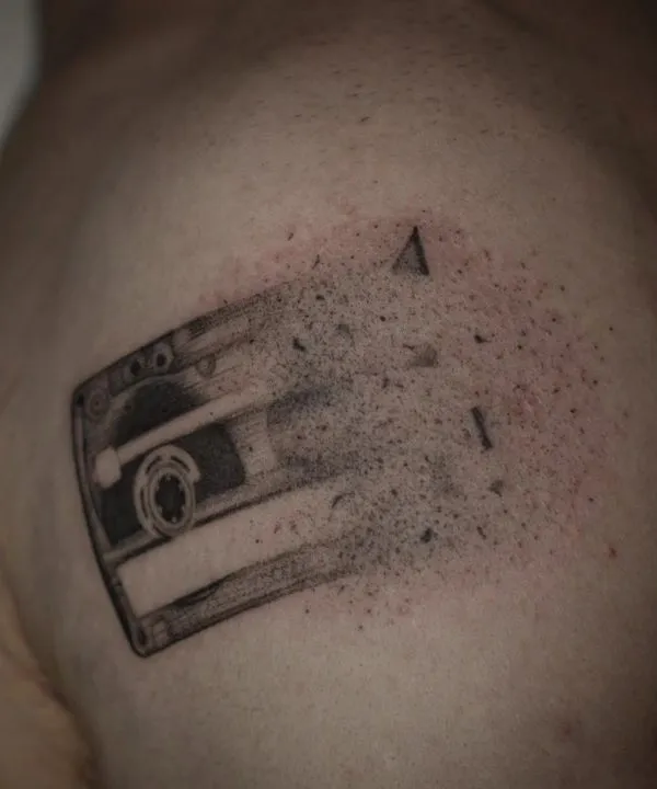 Kaseta magnetofonowa rozsypująca się w kropki, dotwork na ramieniu.
